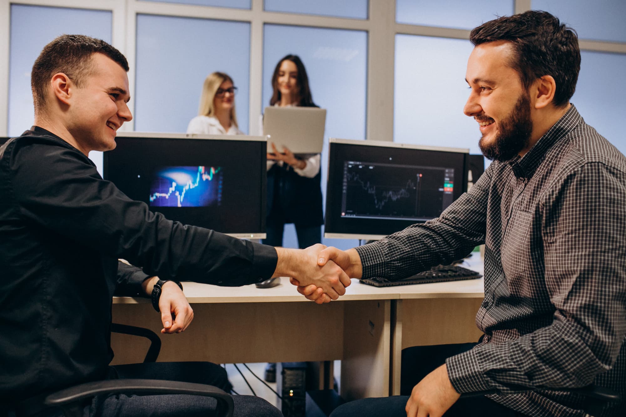 Two men are smiling and shaking hands at a desk in an office in Minnesota over a managed IT and cybersecurity partnership deal for their B2B service company